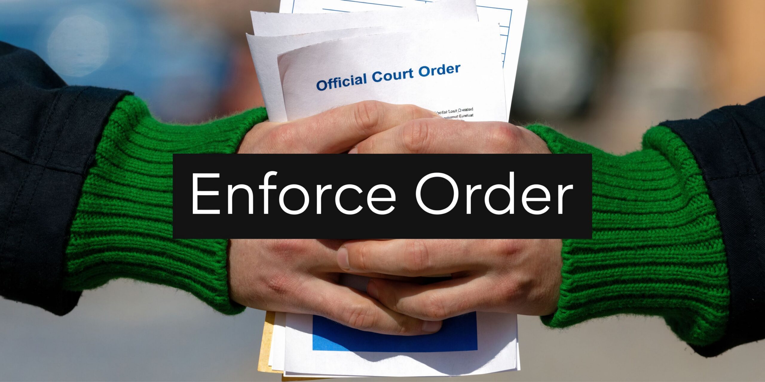 Close-up view of person's hands holding stacks of official court order documents outdoors while wearing green sweaters.