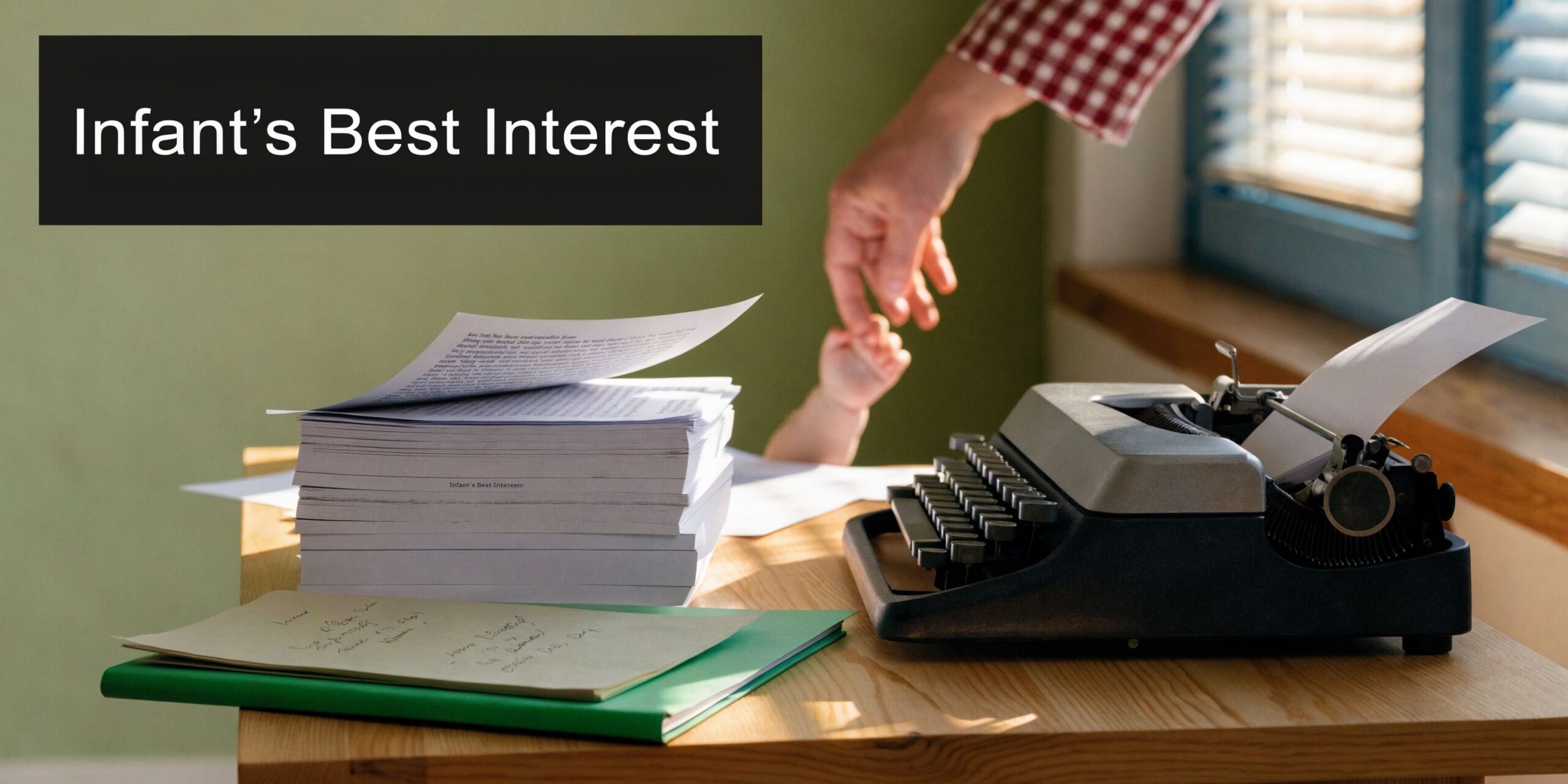 A close-up of a parent's hand holding an infant's tiny hand next to a vintage typewriter.