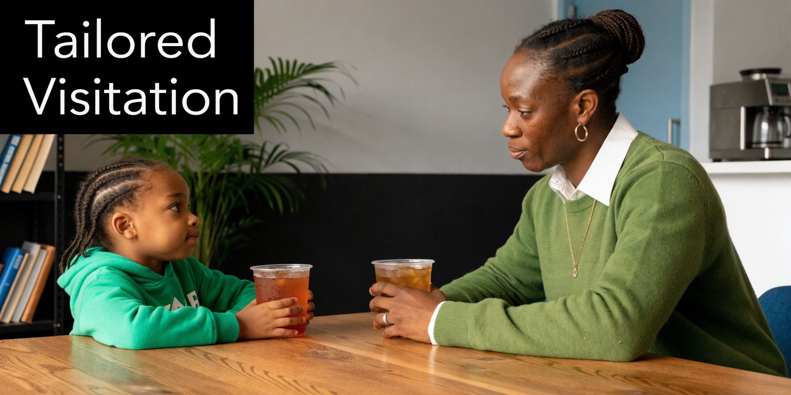 A young child and a woman sitting at a table with drinks during a supervised visitation session.