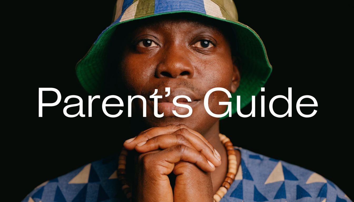 A close-up portrait of a thoughtful man wearing a patterned bucket hat and beads against black.