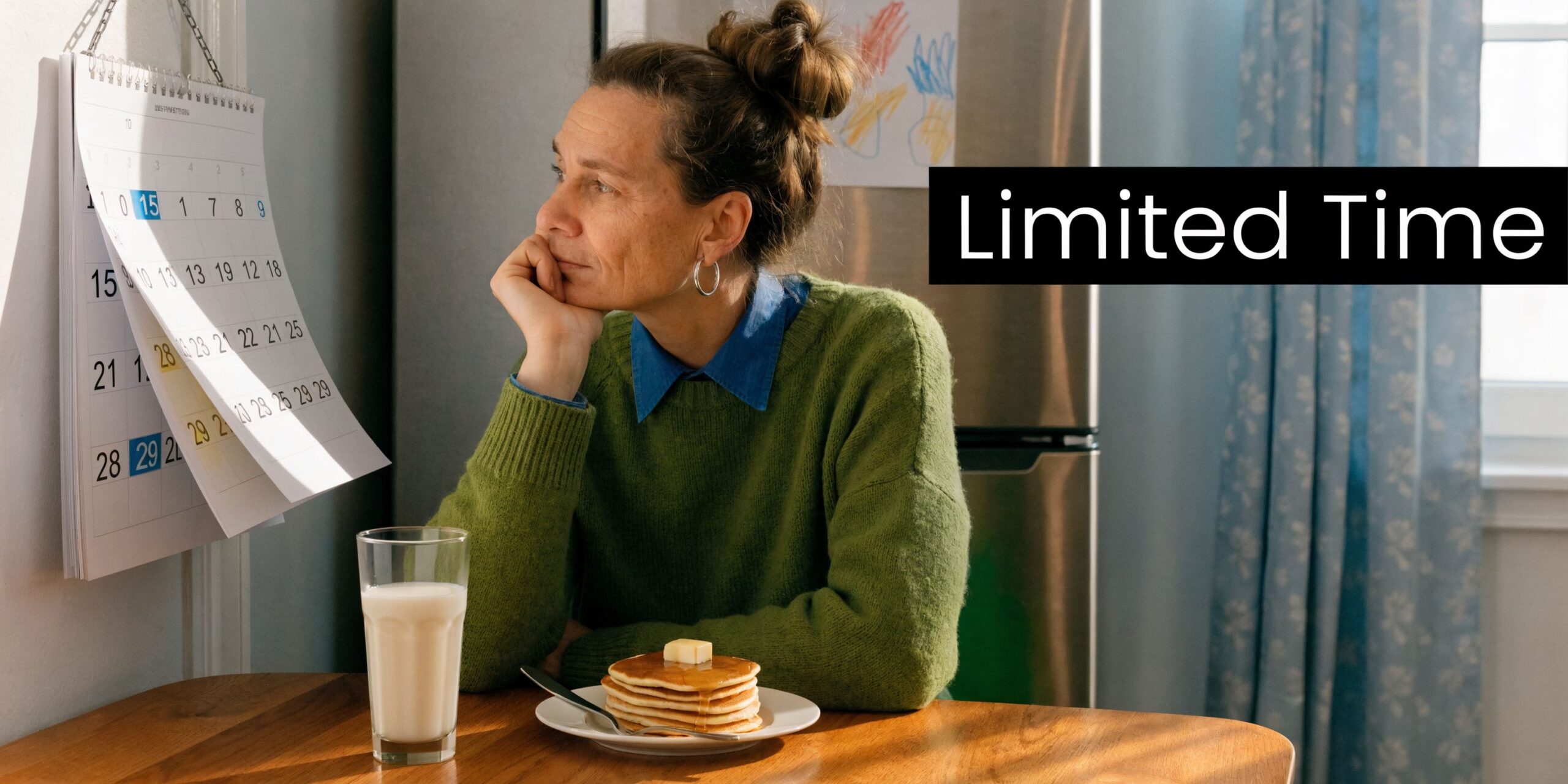 A pensive woman sits at a wooden kitchen table with pancakes and milk, looking at a calendar.