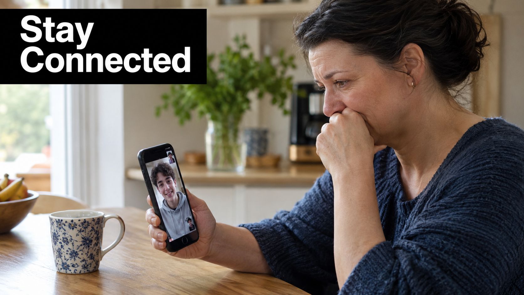 A concerned woman holding a smartphone during a video call with her son in a kitchen setting.